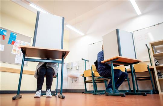 Wähler sitzen in einem Wahlraum in der Lutherschule hinter einem Sichtschutz.