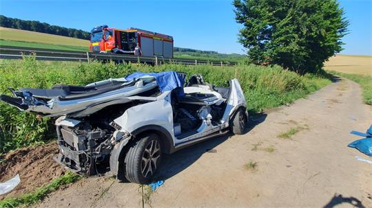 Ein zerqutschtes weißes Auto steht auf einem Feldweg.