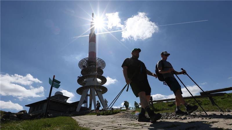 Wanderer gehen bei strahlendem Sonnenschein über einen Weg auf dem Brocken, im Hintergrund steht der Fernmeldeturm. 