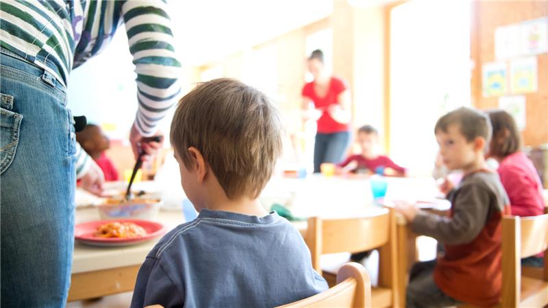 Kinder sitzen in einer Kita und warten, dass ihnen das Essen aufgetan wird.