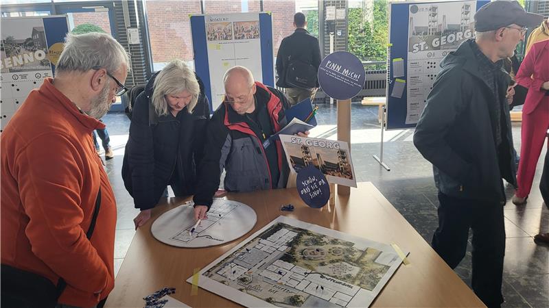 Mehrere Personen stehen an einem Tisch mit Stadtplänen und Informationsmaterial in einem hellen Innenraum