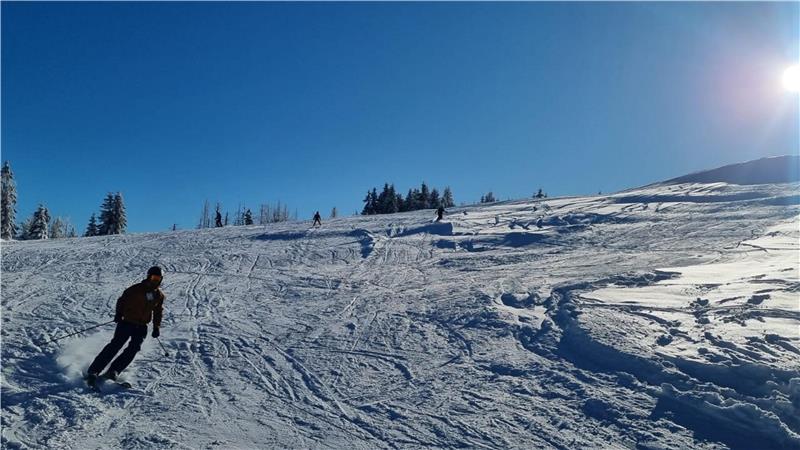 Ein Mann fährt auf Skiern bei Sonnenschein den verschneiten Berg hinunter.