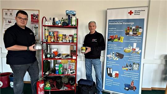 Zwei Männer stehen vor einem Regal mit Waren und einem Informationsplakat des DRK.