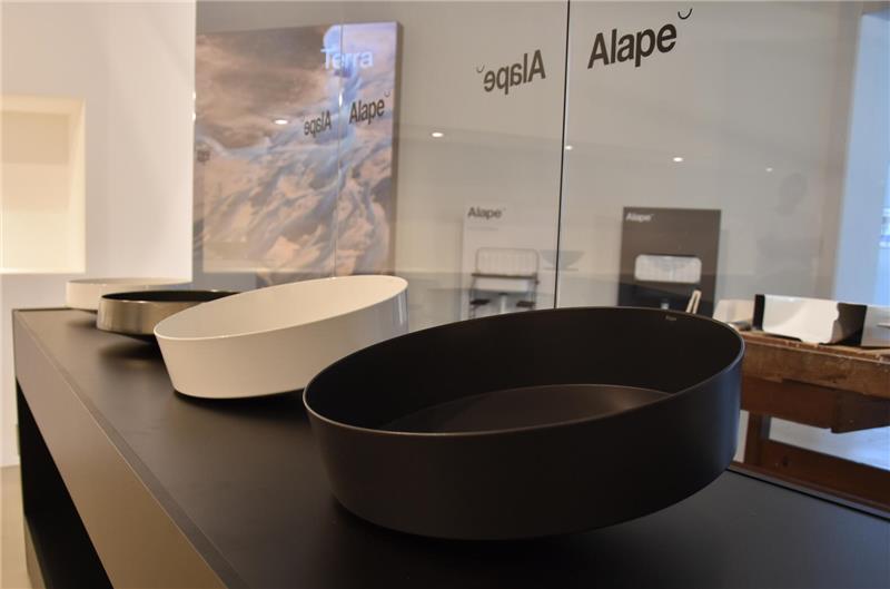 Drei unterschiedlich große, runde Waschbecken in Schwarz, Weiß und Grau auf schwarzer Theke in modernem Ausstellungsraum.