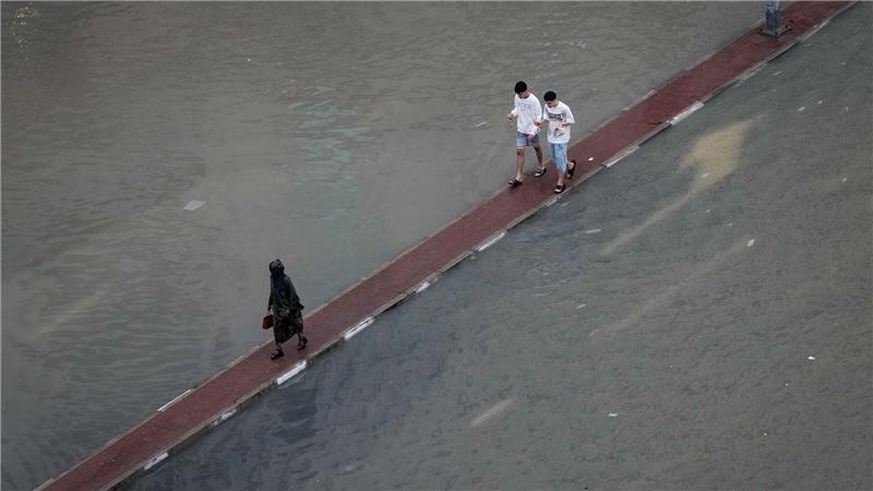 Wasser auf der Fahrbahn: Passanten in Dubai suchen auf dem Fahrbahnteiler einen trockenen Weg nach Unwettern