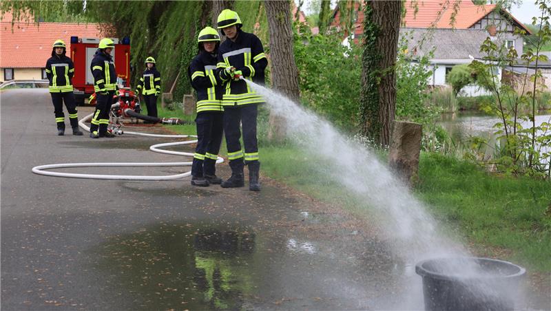 Feuerwehrleute in Schutzkleidung löschen mit Wasserschläuchen einen Brand auf einer Straße
