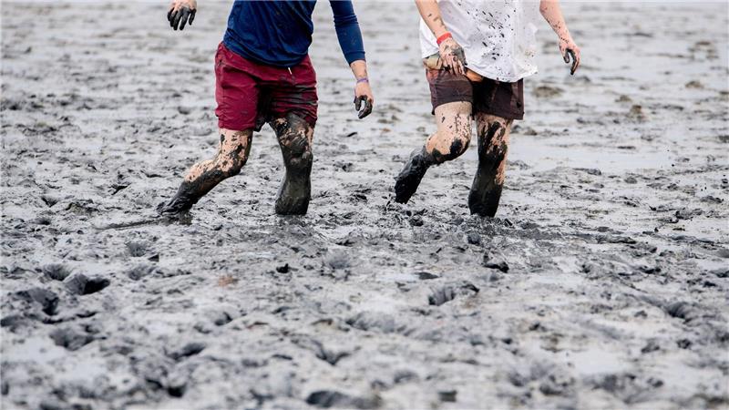 Watt en Schlick Festival - Zwei Teilnehmer gehen bei den deutschen Meisterschaften im Schlickrutschen im Rahmen des Watt en Schlick Fest am Strand von Dangast durch das Watt.