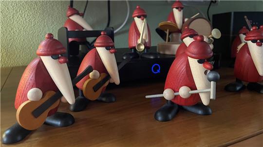 Mehrere hölzerne Weihnachtsmänner mit roten Mützen und roten Gewändern, einige mit Musikinstrumenten wie Gitarre und Trommeln.