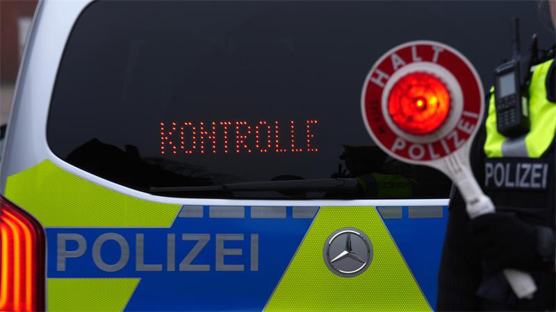 Eine Polizistin hält eine Anhaltekelle vor den Schriftzug „Kontrolle“ an der Heckscheibe des Einsatzfahrzeugs.