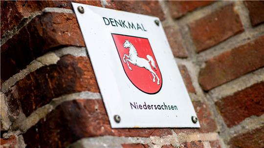 Ein Schild mit dem Wappen von Niedersachsen und der Aufschrift "Denkmal Niedersachsen" hängt an einem Gebäude