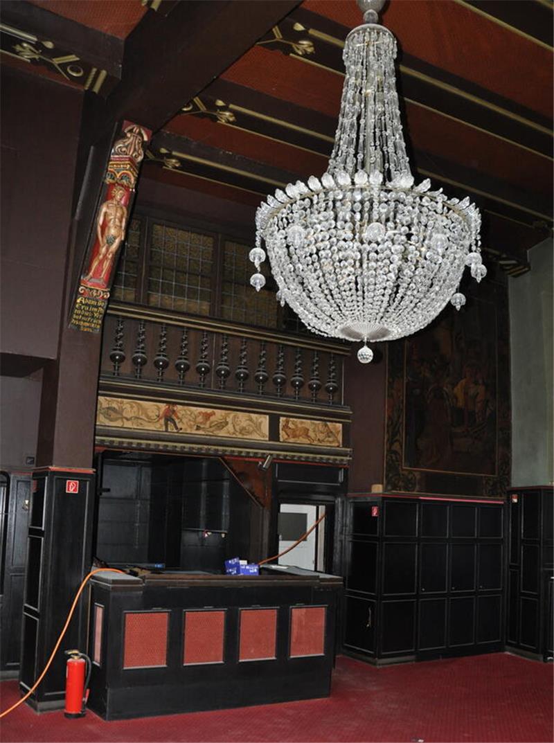 Zwei Goslarer Hotels mit Geschichte – und klaren Zukunftsplänen Großer Kristalllüster hängt in einem Raum mit dunklen Holzpaneelen, rotem Teppich und einer Holzfigur an der Wand.