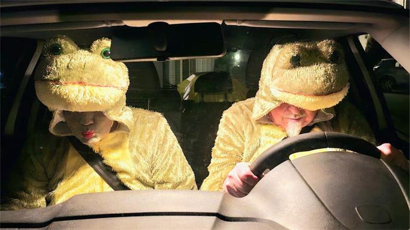 Zwei Personen in gelben Tierkostümen sitzen in einem Auto, eine Person am Steuer, die andere auf dem Beifahrersitz.