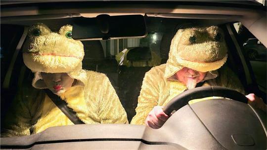 Zwei Personen in gelben Tierkostümen sitzen in einem Auto, eine Person am Steuer, die andere auf dem Beifahrersitz.