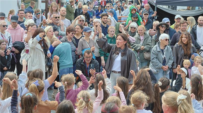 Menschenmenge bei einer Veranstaltung mit vielen Kindern im Vordergrund, die die Arme heben, und Erwachsenen im Hintergrund vor Marktständen
