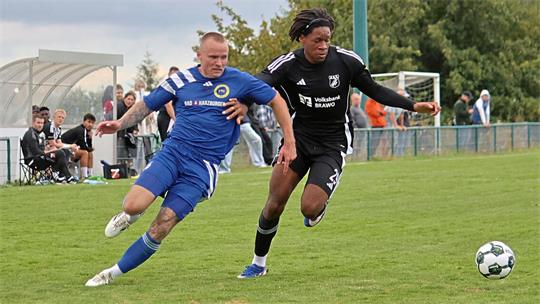 Zwei Fußballspieler in blauer und schwarzer Spielkleidung kämpfen um den Ball auf dem Spielfeld