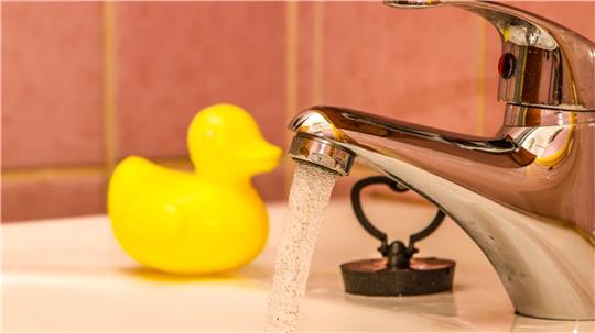 Wasser läuft aus einem Wasserhahn. Es ist auch eine Quietscheente zu sehen.