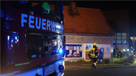 Ein Feuerwehrfahrzeug steht vor einem ehemaligen Imbissgebäude. Ein Feuerwehrmann läuft auf das Gebäude zu.
