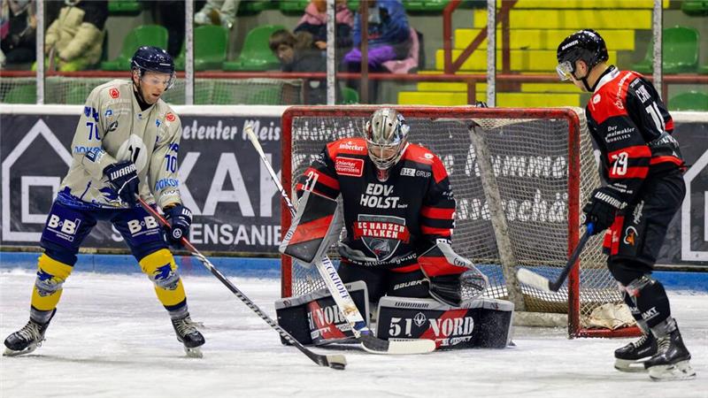 Eishockeyszene mit Torwart in schwarzem Trikot und zwei Spielern, einer in weiß-blauem und einer in schwarz-rotem Trikot, vor dem Tor auf dem Eis.