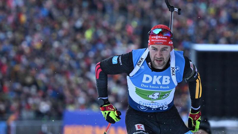 Langläufer mit roter Mütze, schwarzem Anzug und blauem Wettkampfhemd mit DKB-Logo beim Skilanglauf vor Zuschauermenge