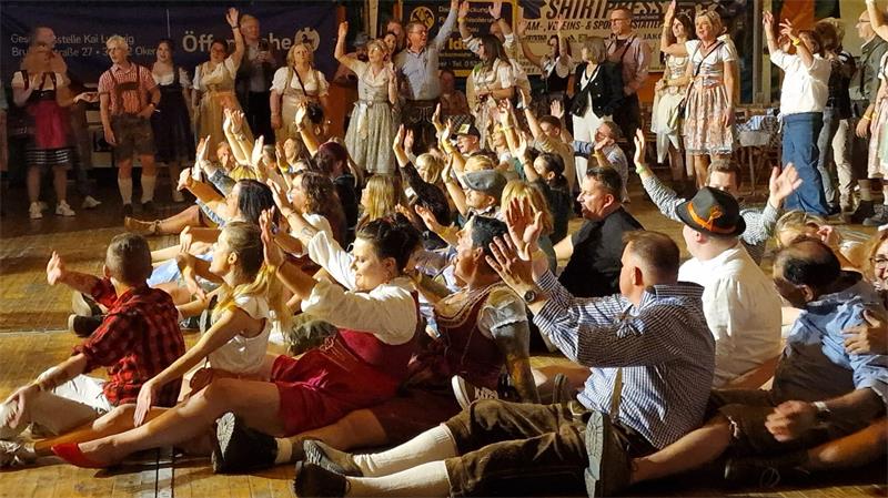 Gruppe von Menschen in traditioneller Tracht sitzt auf dem Boden und hebt die Arme in die Luft