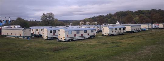 Zirkusgelände mit zahlreichen Wohn- und Transportwagen auf einer Wiese, im Hintergrund das große Zirkuszelt.