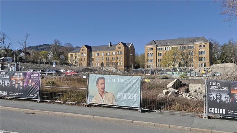 Bauzaun mit Werbebannern vor einem großen historischen Backsteingebäude unter blauem Himmel