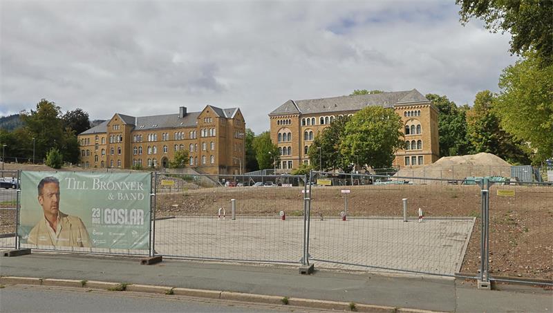 Baustelle mit Baugrube und Bauzaun vor historischen Backsteingebäuden unter bewölktem Himmel