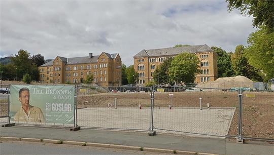 Baustelle mit Baugrube und Bauzaun vor historischen Backsteingebäuden unter bewölktem Himmel