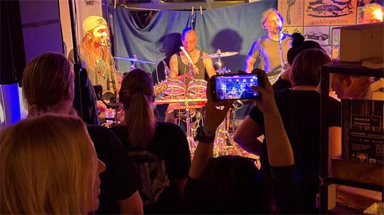 Das Foto zeigt eine Band auf der Bühne und einen Fan, der sie mit dem Handy fotografiert.