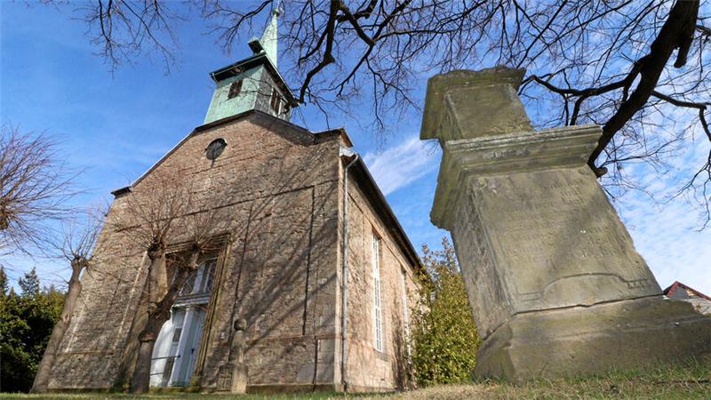 Eine Kirche unter blauem Himmel mit einem Gedenkstein im Vordergrund.