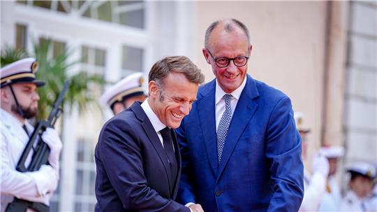 Wie zwei alte Freunde begrüßen sich Macron und Merz vor dem Fort du Cap Brun über der Cote d’Azur.