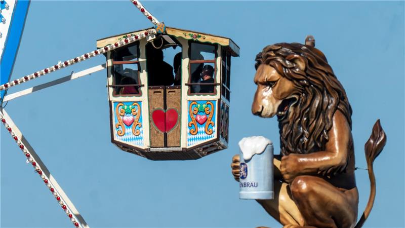 Wiesn-Besucher fahren in einem Riesenrad auf dem 190. Münchner Oktoberfest an der Kulisse einen überdimensionalen Löwen mit Bierkrugs vorbei.