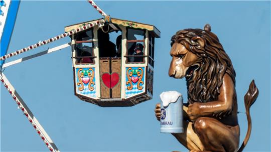 Wiesn-Besucher fahren in einem Riesenrad auf dem 190. Münchner Oktoberfest an der Kulisse einen überdimensionalen Löwen mit Bierkrugs vorbei.