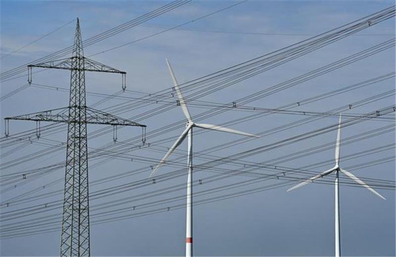 Windenergieanlagen stehen hinter Hochspannungsmasten. Unternehmer aus unserer Region beklagen die Folgen stark steigender Energiepreise. Foto: Patrick Pleul/dpa