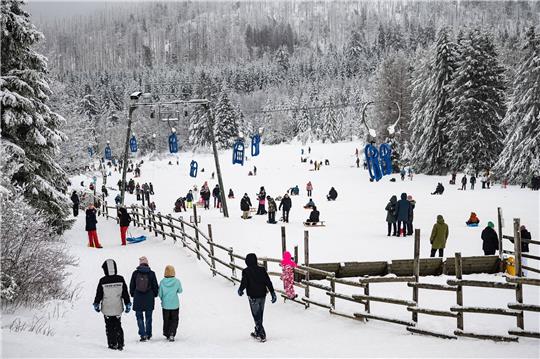 Wintersportler gehen mit ihren Schlitten an einem Rodellift im Harz entlang.