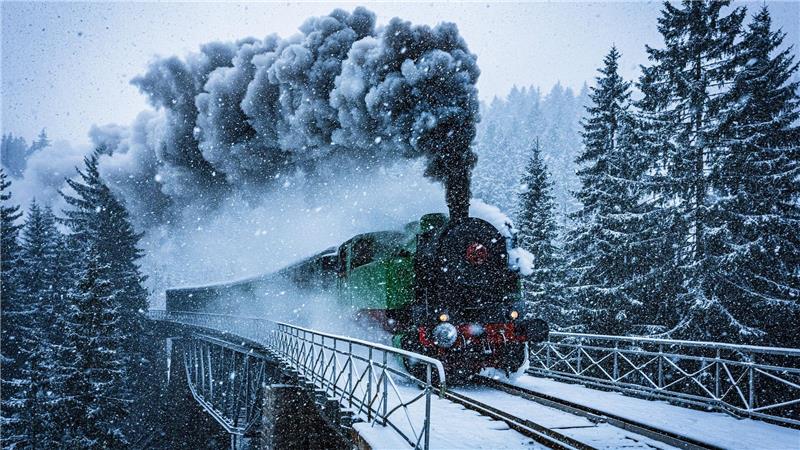 Winterwunderwelt: Eine historische Dampflokomotive fährt in Tschechien durch die verschneite Landschaft.
