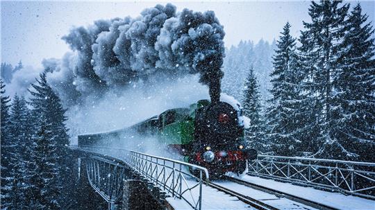 Winterwunderwelt: Eine historische Dampflokomotive fährt in Tschechien durch die verschneite Landschaft.
