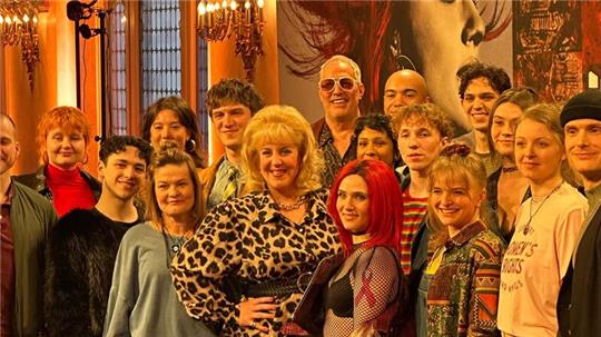 Gruppe von Menschen in einem prunkvollen Raum mit hohen Fenstern und Kronleuchtern