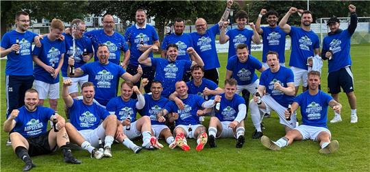 Gruppenfoto von Fußballspielern in blauen Trikots auf einem Spielfeld vor Bäumen und bewölktem Himmel