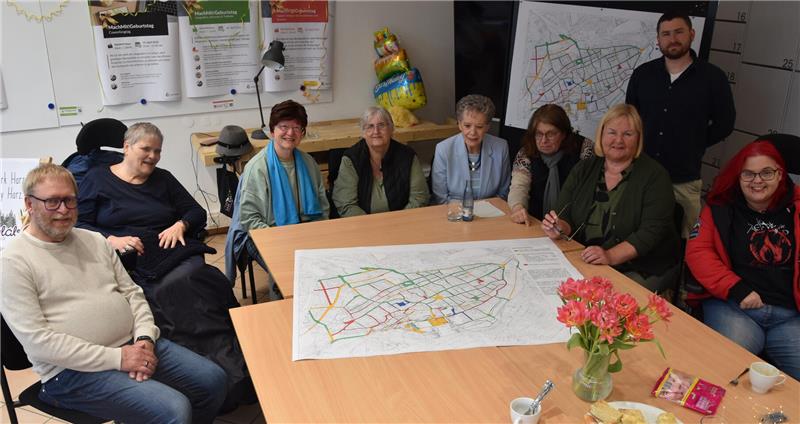Gruppe von Menschen sitzt um einen Tisch mit einer großen Karte darauf in einem Raum mit Informationsplakaten an der Wand.