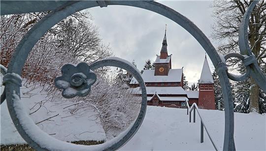 Verschneite Stabkirche hinter einem eisbedeckten, schmiedeeisernen Tor mit Blütenornament