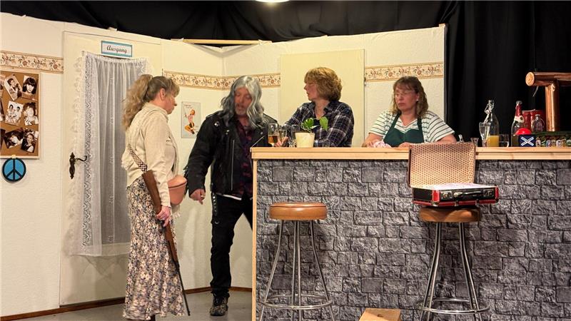 Das Foto zeigt eine Frau mit einem Gewehr und drei weitere Personen, die an einer Theke stehen.