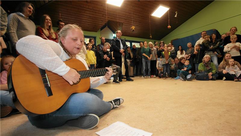 Zahlreiche Besucher finden sich zur Eröffnungsfeier ein, bei der Kita-Leiterin Lydia Ursel die Kinder auf der Gitarre begleitet.