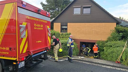 Feuerwehrfahrzeug mit Aufschrift 'FEUERWEHR OTHFRESEN' und mehreren Einsatzkräften vor einem Wohnhaus mit offener Kellertür