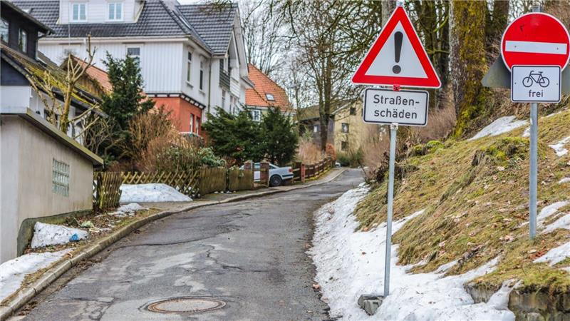 Schmale Straße mit Schlaglöchern und zwei Verkehrsschildern, eines warnt vor Straßenschäden, das andere zeigt Einfahrt verboten mit Zusatz "frei" für Fahrräder.