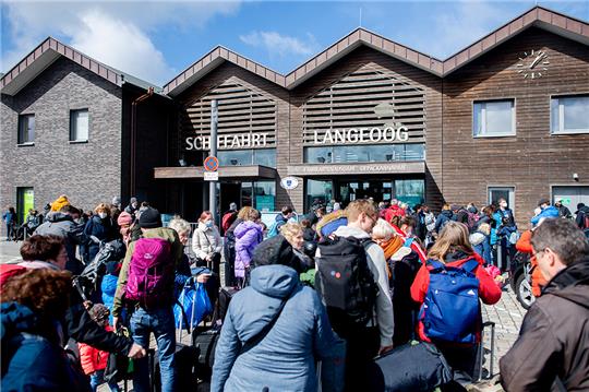 Zahlreiche Touristen warten mit ihrem Gepäck vor dem Fährterminal zur Überfahrt auf die Insel Langeoog. Mit dem Start der Ferien in vielen Bundesländern, darunter Nordrhein-Westfalen, sind am Samstag viele Osterurlauber an die Küste und auf die Ostfriesischen Inseln gereist. Foto: Hauke-Christian Dittrich/dpa