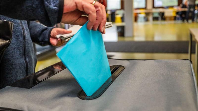 Jemand steckt einen Wahlzettel in die Wahlurne.