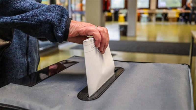 Hand steckt Wahlzettel in die Urne.