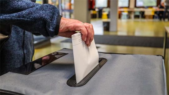 Hand steckt Wahlzettel in die Urne.