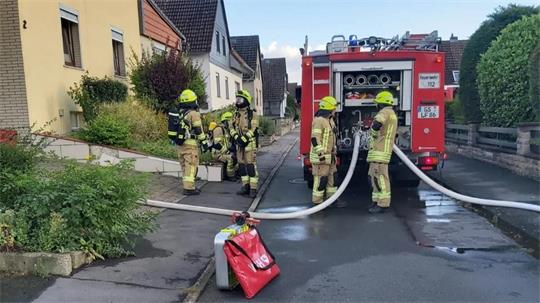 Feuerwehrleute in Schutzkleidung bedienen einen Löschwagen auf einer Wohnstraße mit Reihenhäusern